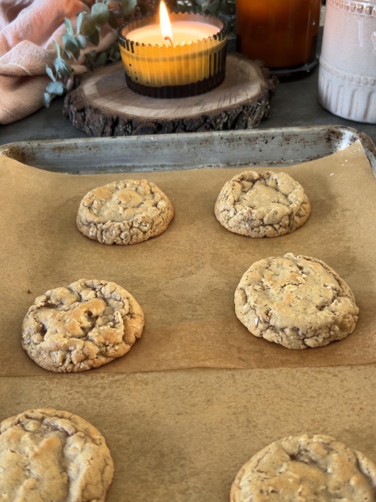 A parchment-paper lined cookie sheet has six baked oatmeal cookies on it.
