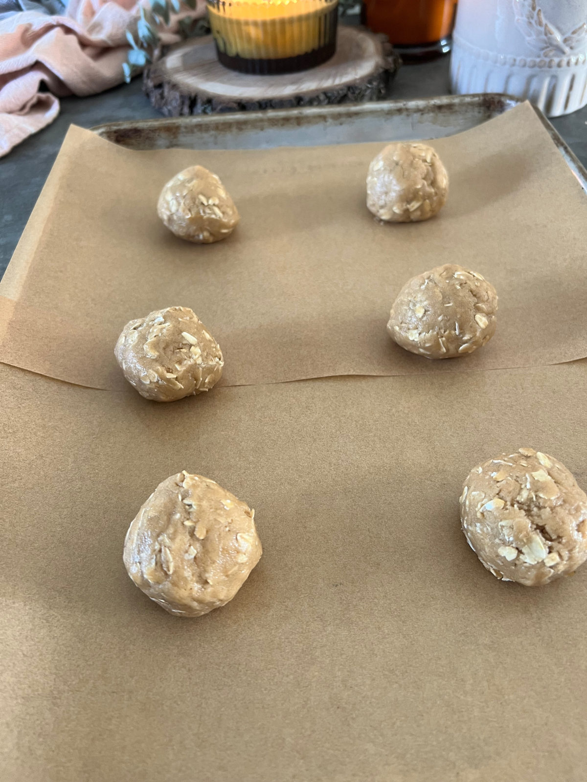 A parchment-lined baking sheet has six oatmeal cookie dough balls on it ready to be baked.