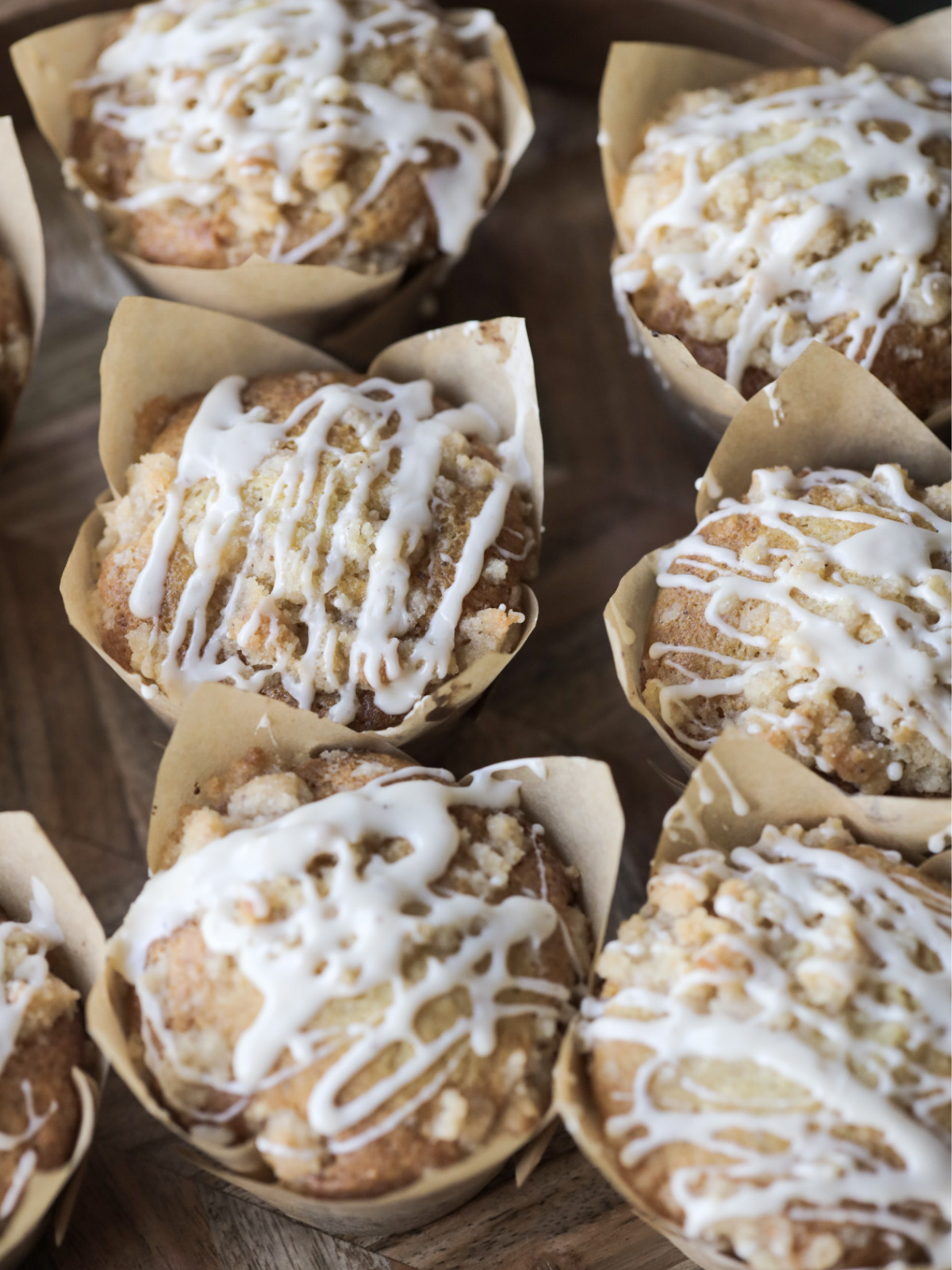 Six vanilla bean sourdough muffins with crumble topping and vanilla bean icing sit on a wooden platter.