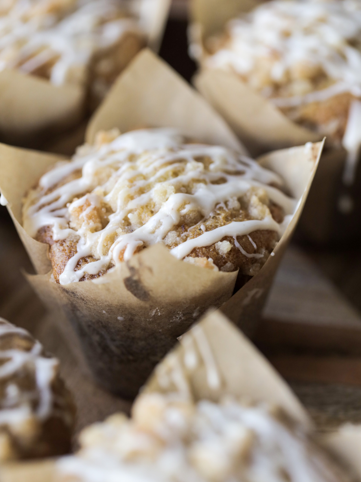 A closeup of one sourdough discard vanilla bean muffin with a crumble topping and vanilla bean icing. Several other muffins sit in the background.