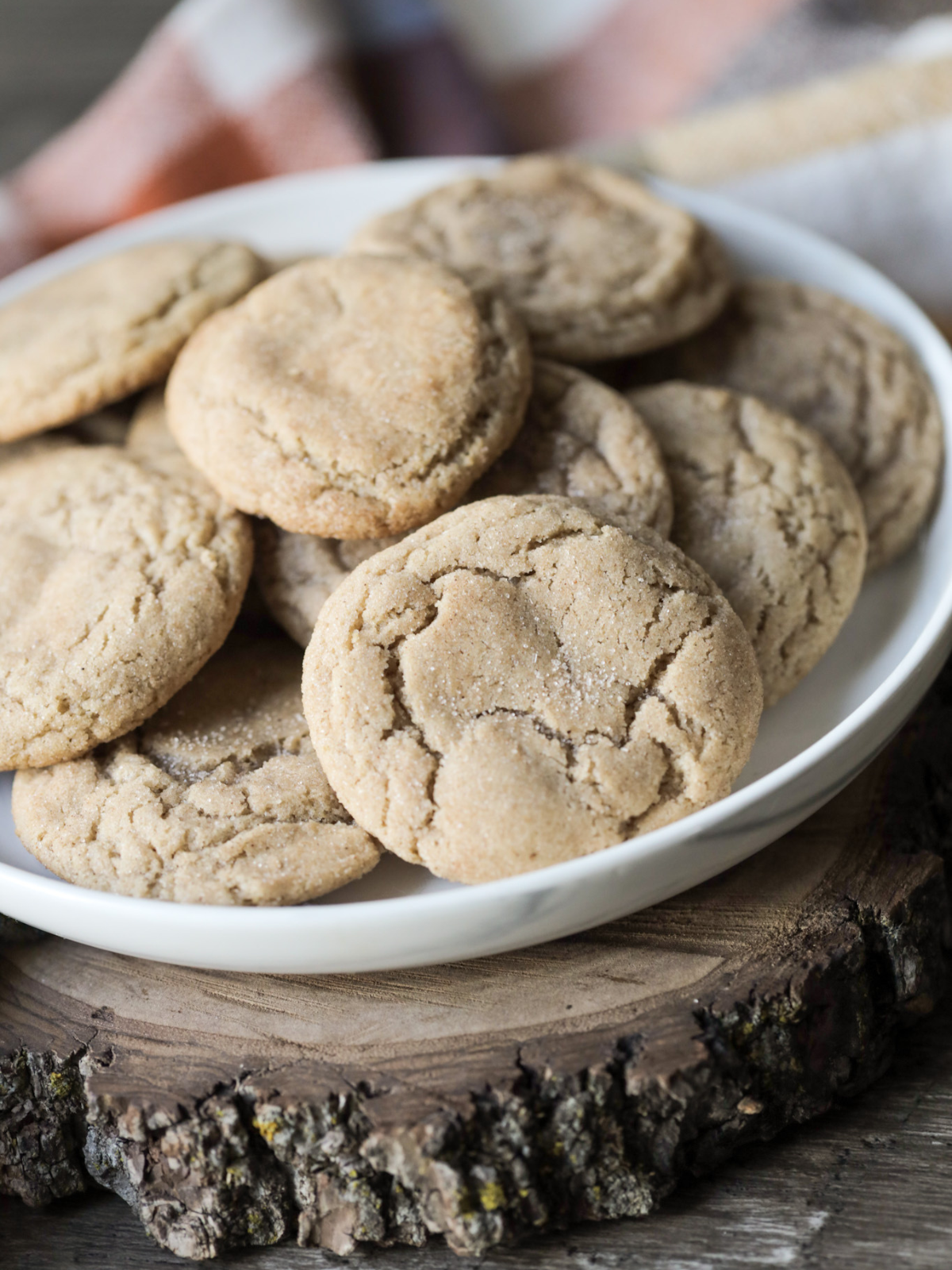 A plate of sourdough snickerdoodle cookies sit on a wooden slab with a kitchen towel in the background.