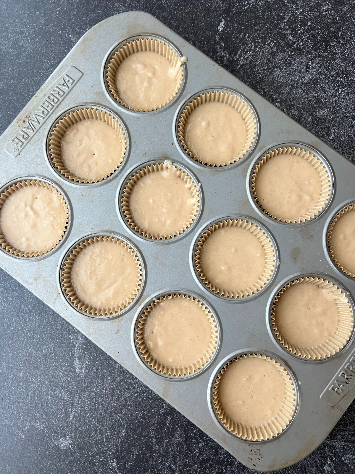 A muffin tin holds the cupcake batter for these sourdough snickerdoodle cupcakes. They are lined with a natural cupcake liner. 