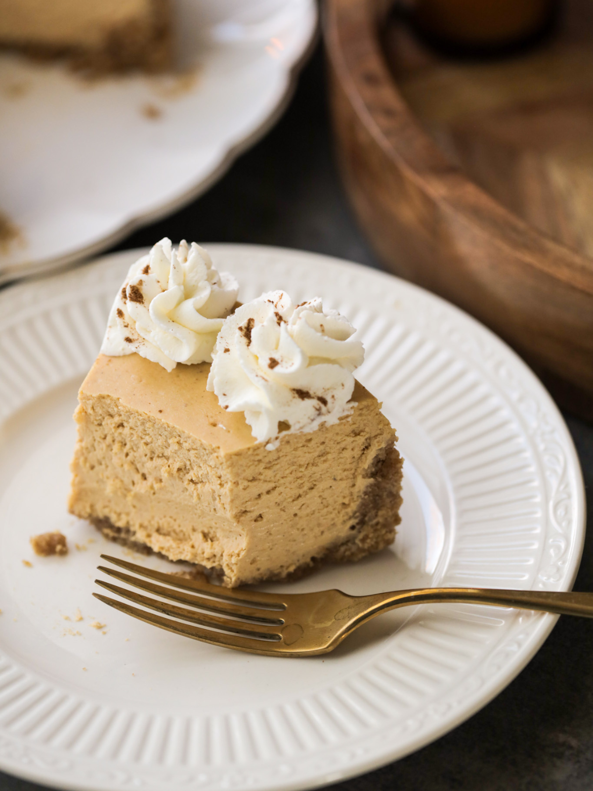 A half eaten slice of pumpkin cheesecake sits on a plate with a golden fork. 