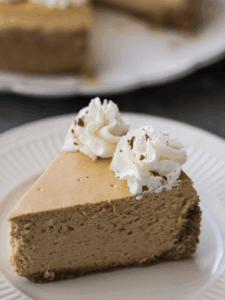 A slice of homemade pumpkin cheesecake sits on a plate with whipped topping on the slice of cheesecake.