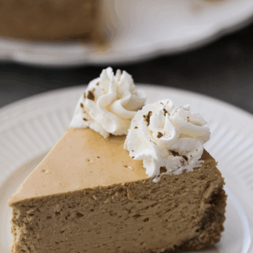 A slice of homemade pumpkin cheesecake sits on a plate with whipped topping on the slice of cheesecake.