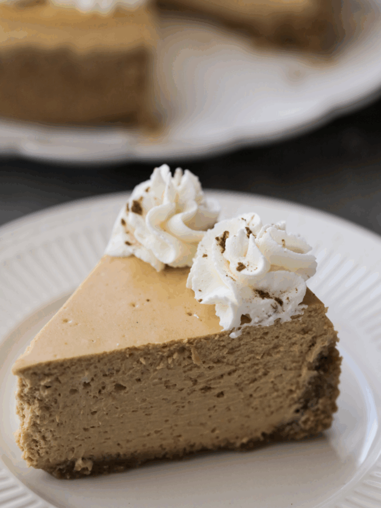 A slice of homemade pumpkin cheesecake sits on a plate with whipped topping on the slice of cheesecake.