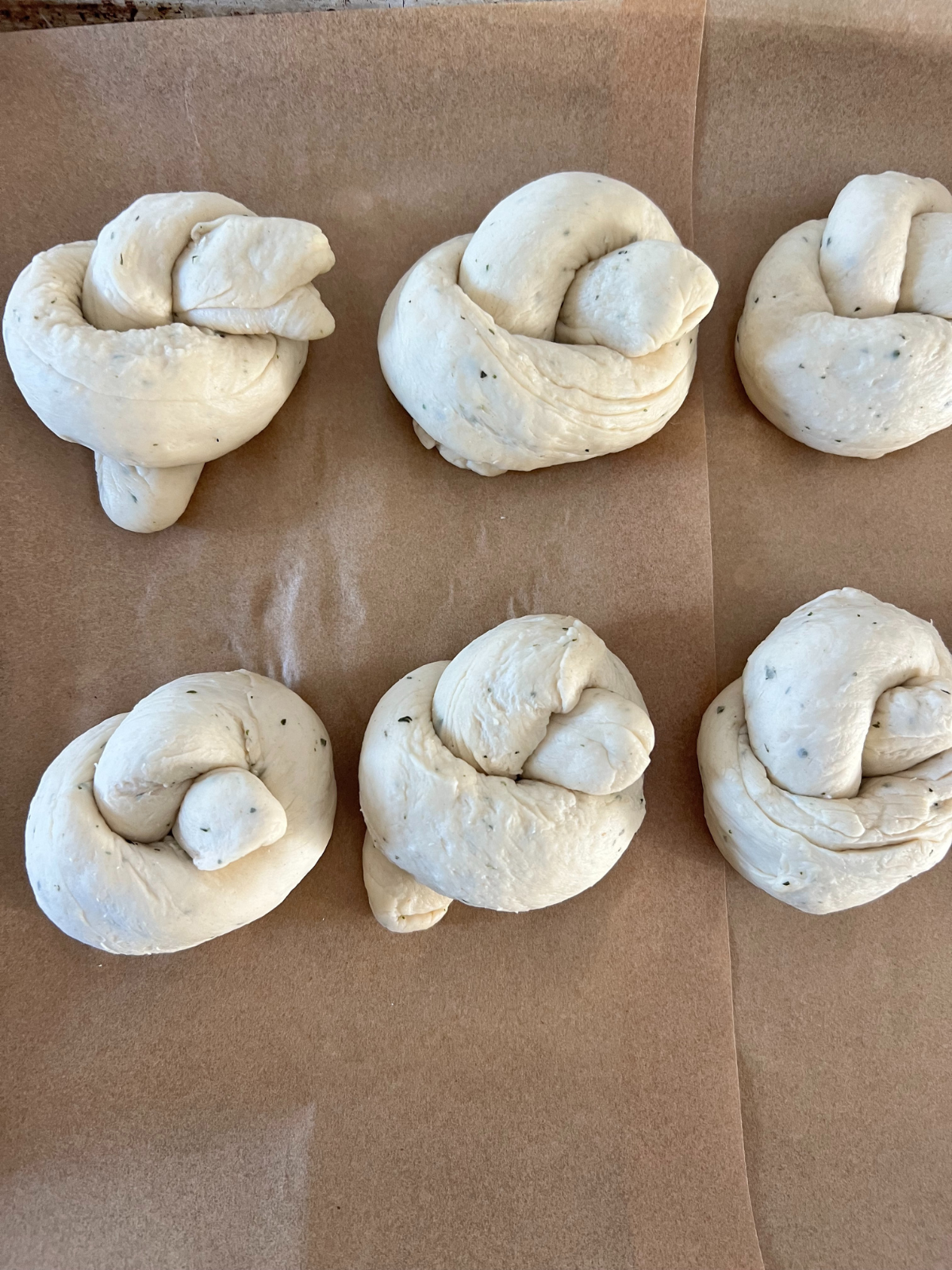 The dough knots sit on the baking sheet as they rise.