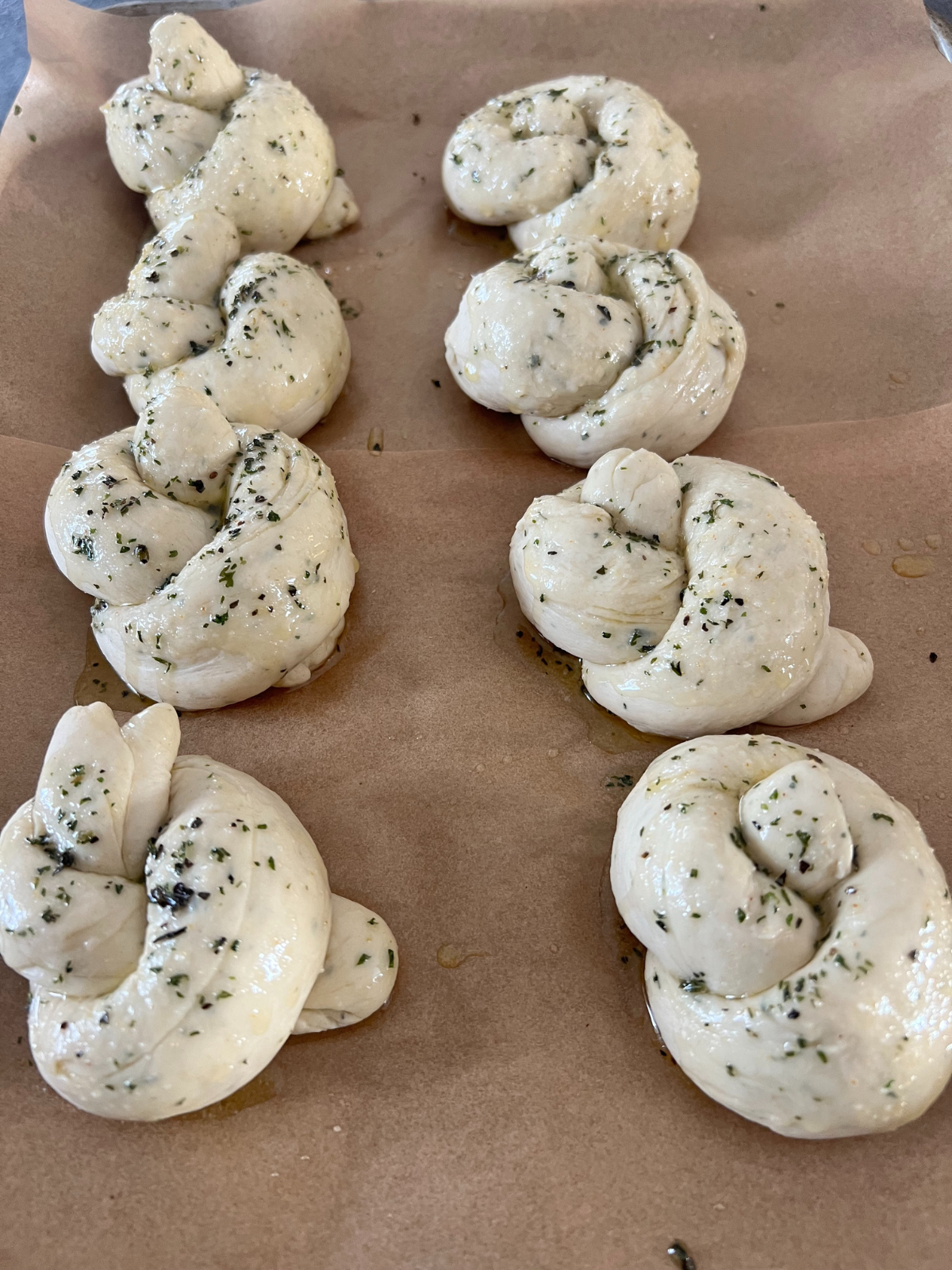 The sourdough knot dough sits on the baking sheet after being brushed with the garlic herb butter.