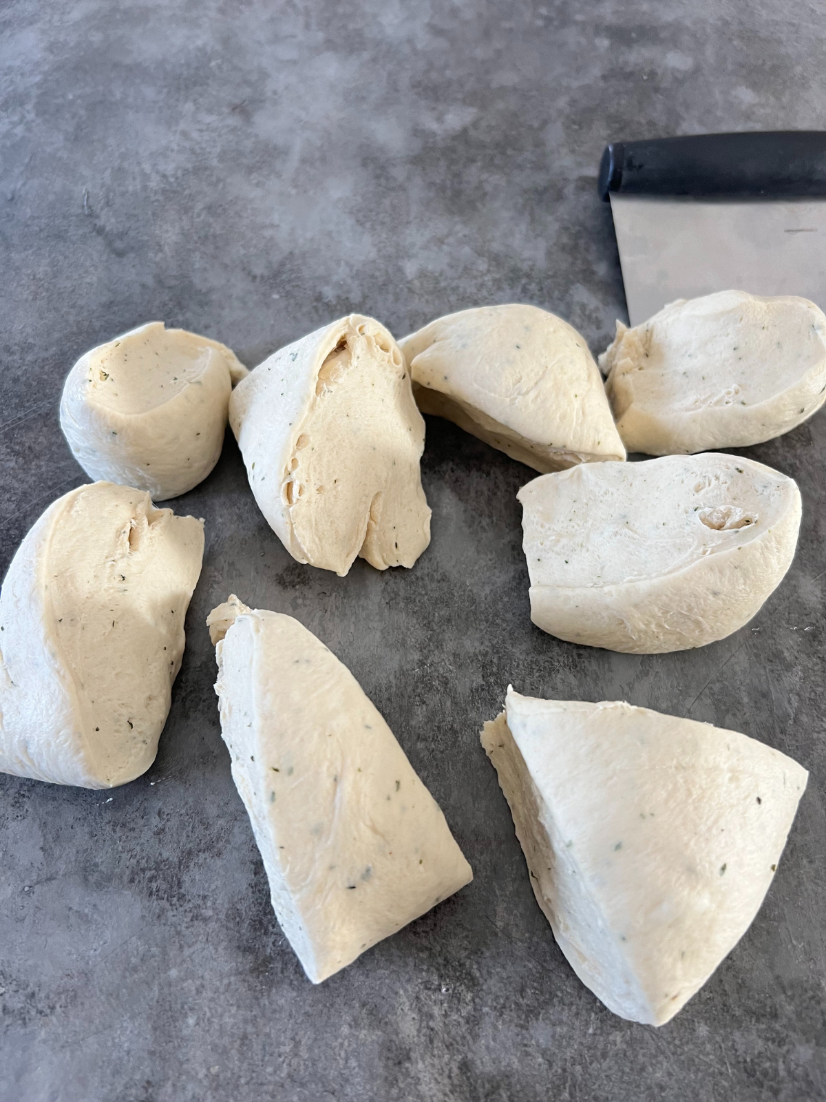 The sourdough garlic and herb knot dough is on a counter separated into 8 pieces.
