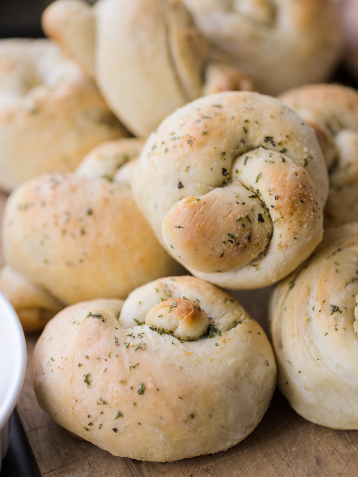 A closeup of freshly baked sourdough garlic knots just out of the oven sit on a wooden cutting board.