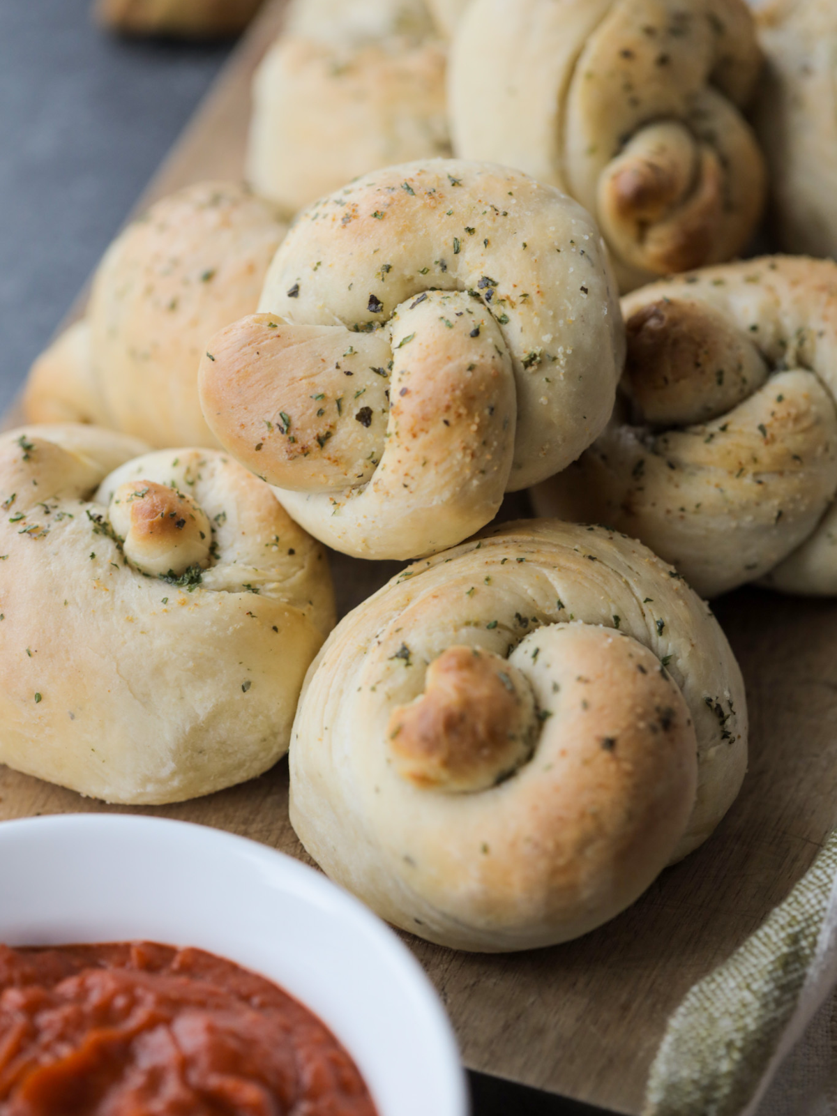 A closeup of sourdough garlic and herb knots with a bowl of marinara in the foreground.