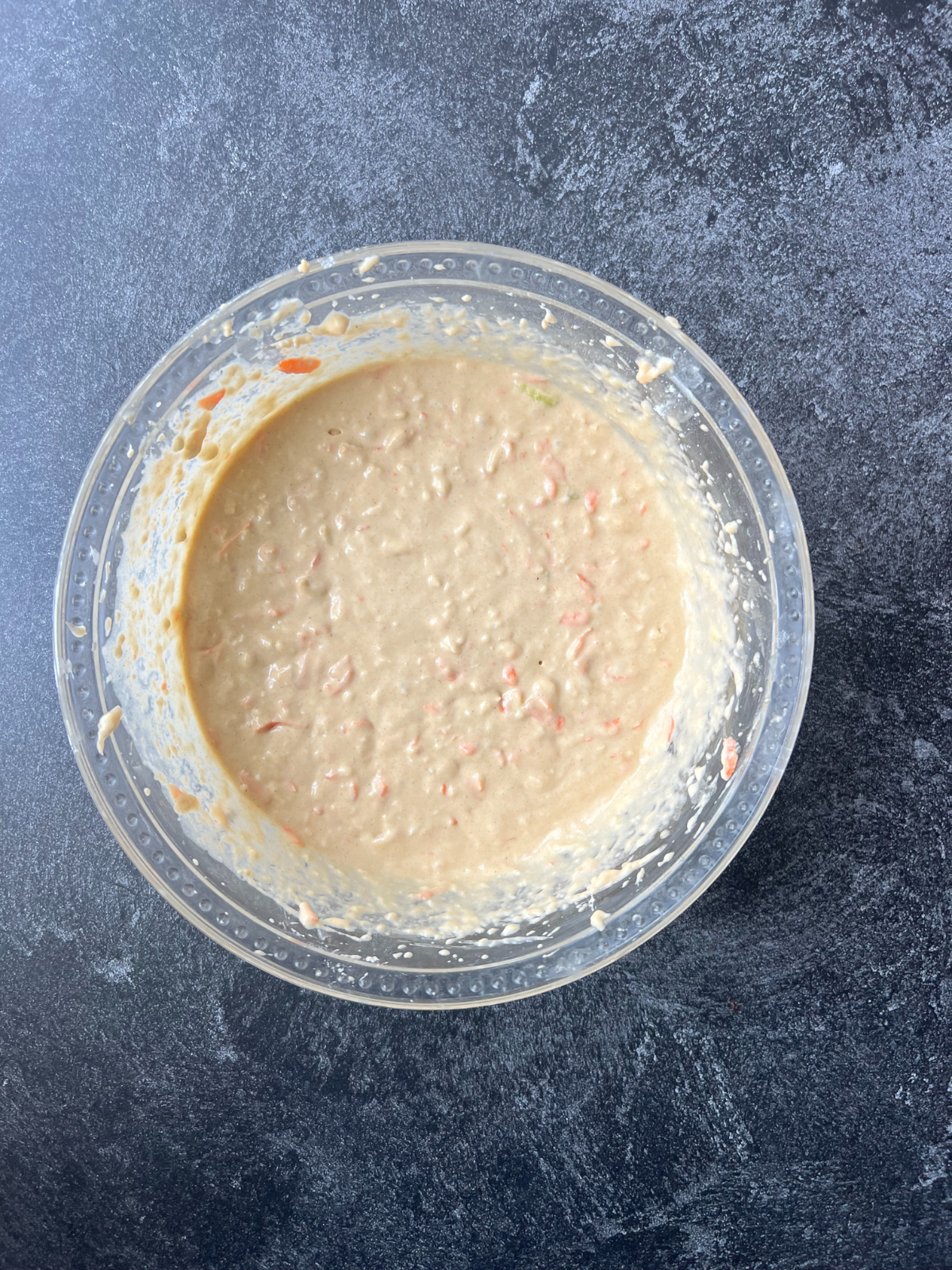 A glass bowl sits with the muffin batter for the carrot apple sourdough muffins.
