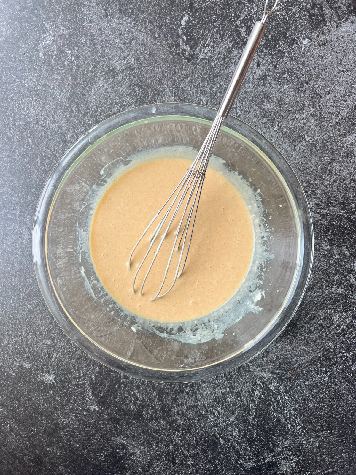 A glass bowl sits with the wet ingredients used for the sourdough carrot apple muffins.