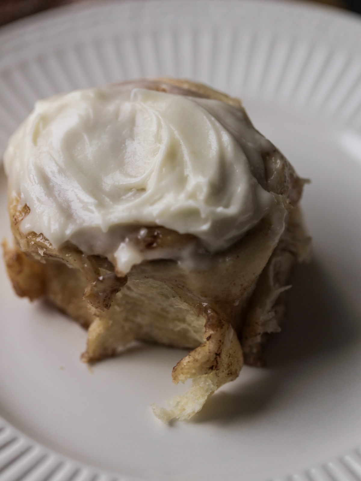 One frosted brioche sourdough cinnamon roll sits on a plate. 