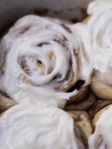 A sourdough brioche cinnamon roll sits warm in the baking pan with cream cheese frosting on top.