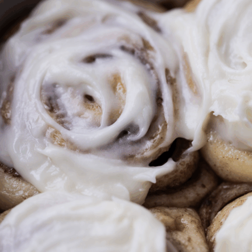 A sourdough brioche cinnamon roll sits warm in the baking pan with cream cheese frosting on top.
