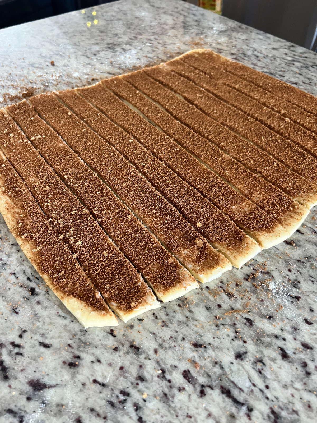 The cinnamon roll dough has been sliced and is ready to roll up. 