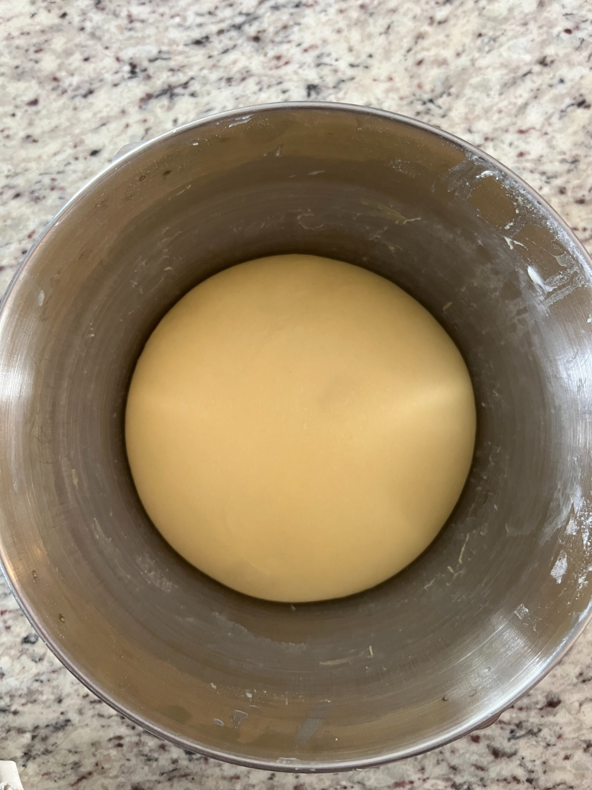 The fermented sourdough cinnamon roll dough sits in a metal mixing bowl. It has risen by about 50%.
