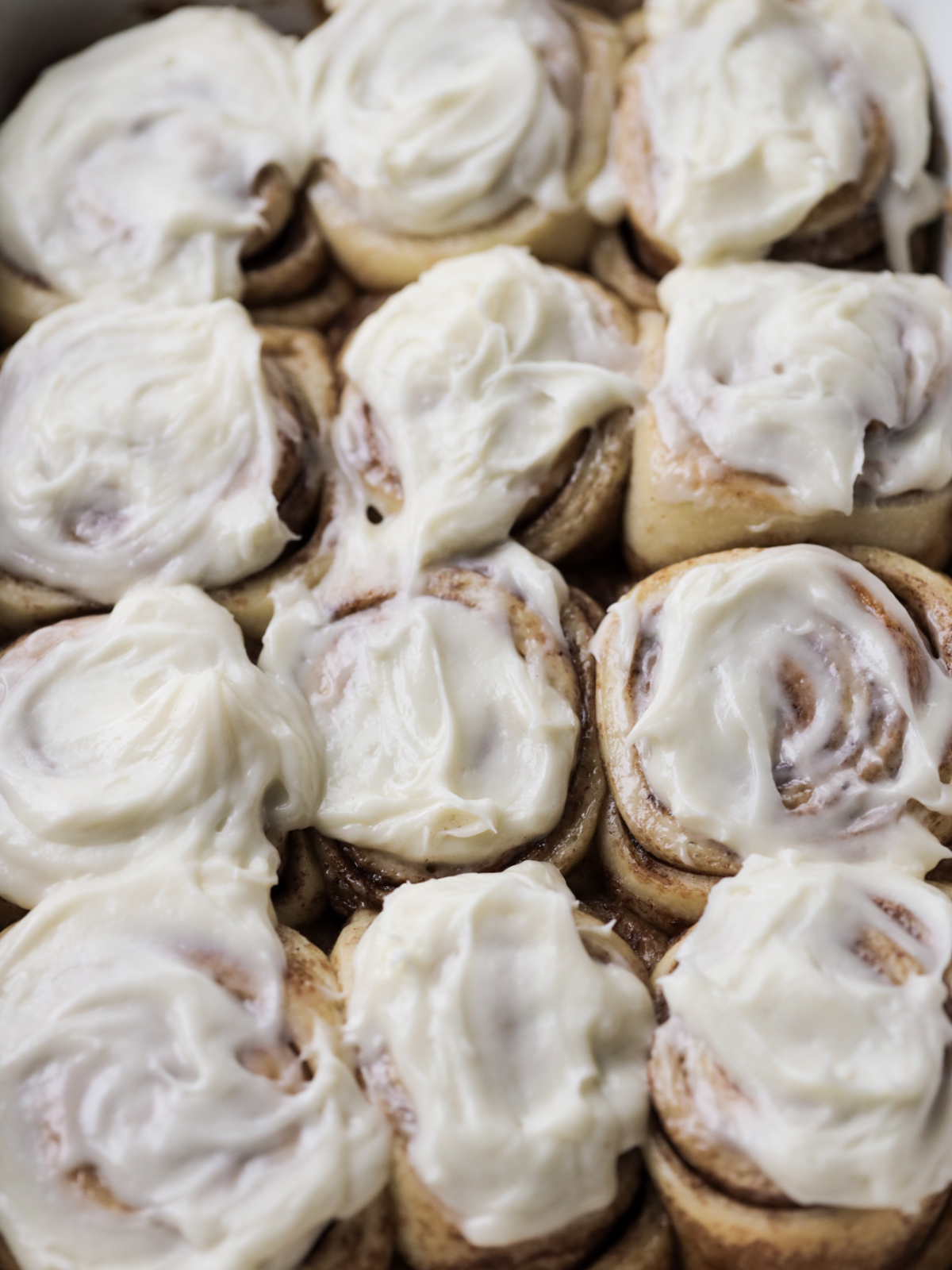 Twelve cream cheese frosting sourdough brioche cinnamon rolls sit in a 9x13 inch baking dish.