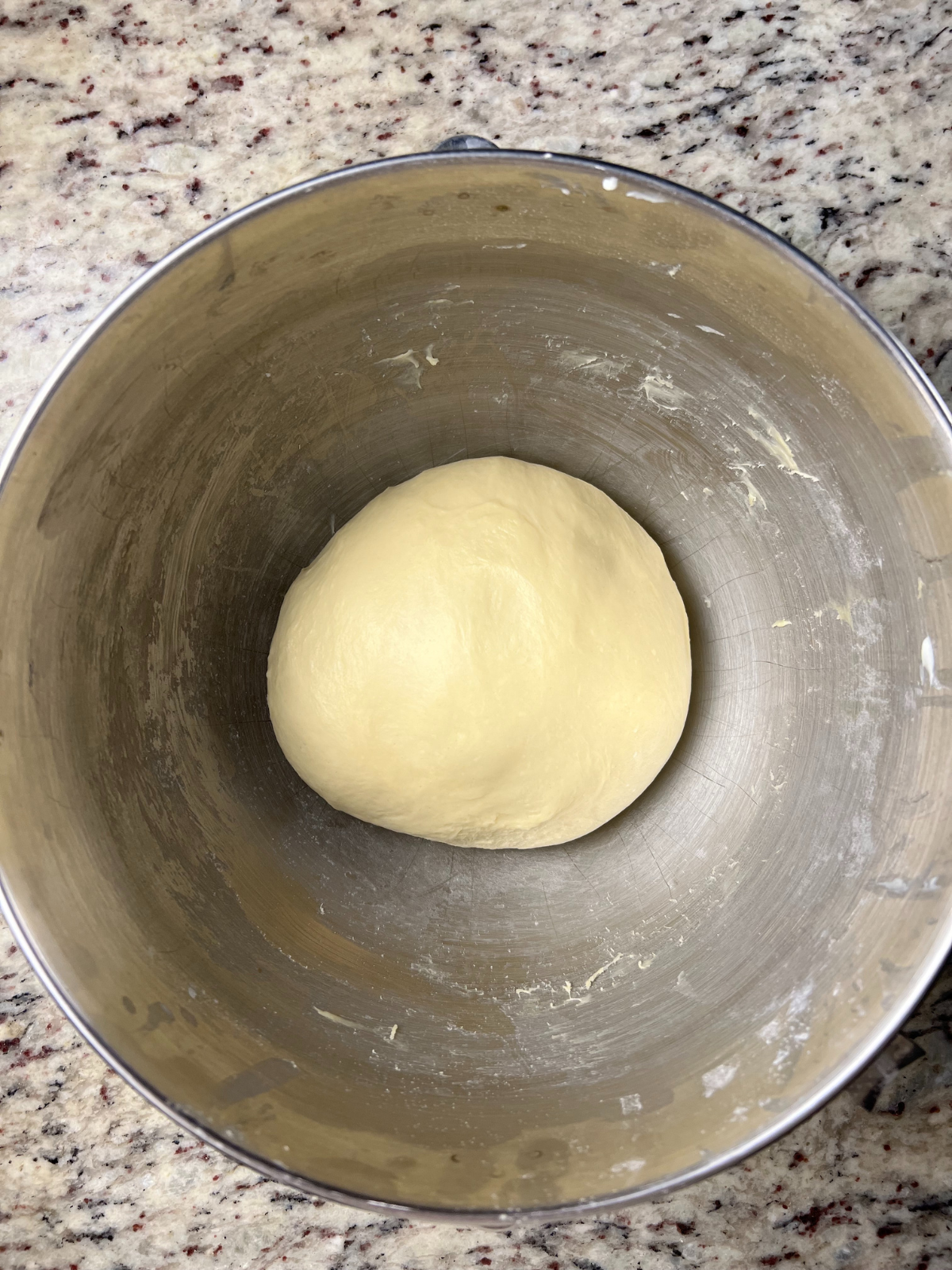 A ball of kneaded sourdough brioche cinnamon roll dough sits in a metal mixing bowl.