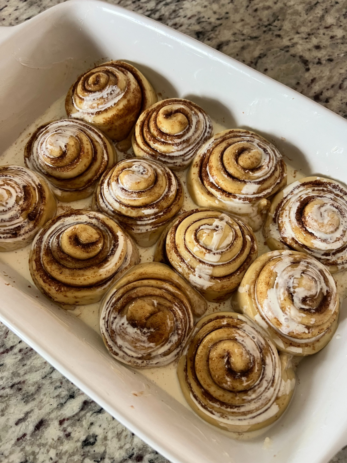 The sourdough cinnamon rolls have risen and have heavy cream poured over them. This will help retain moisture in the rolls.