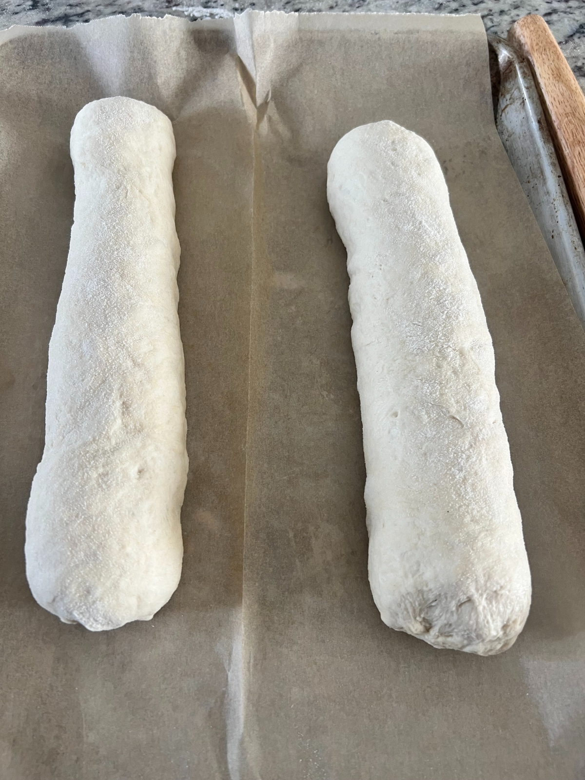 Two loaves of sourdough French bread sit on a parchment paper lined baking sheet. 