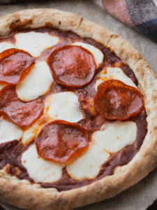 A close up of freshly baked sourdough pizza crust with pepperoni and mozzarella cheese.
