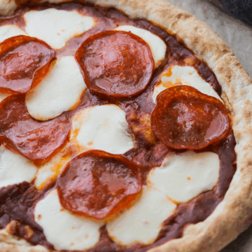 A close up of freshly baked sourdough pizza crust with pepperoni and mozzarella cheese.