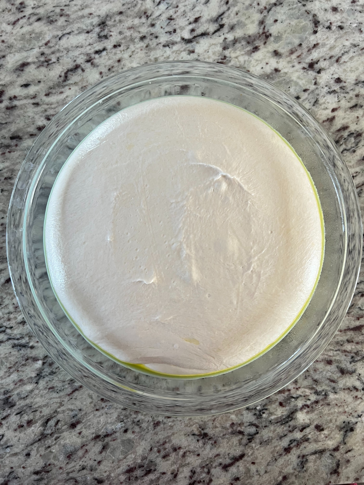 A glass mixing bowl sits on the counter with the full fermented and risen sourdough pizza dough. 
