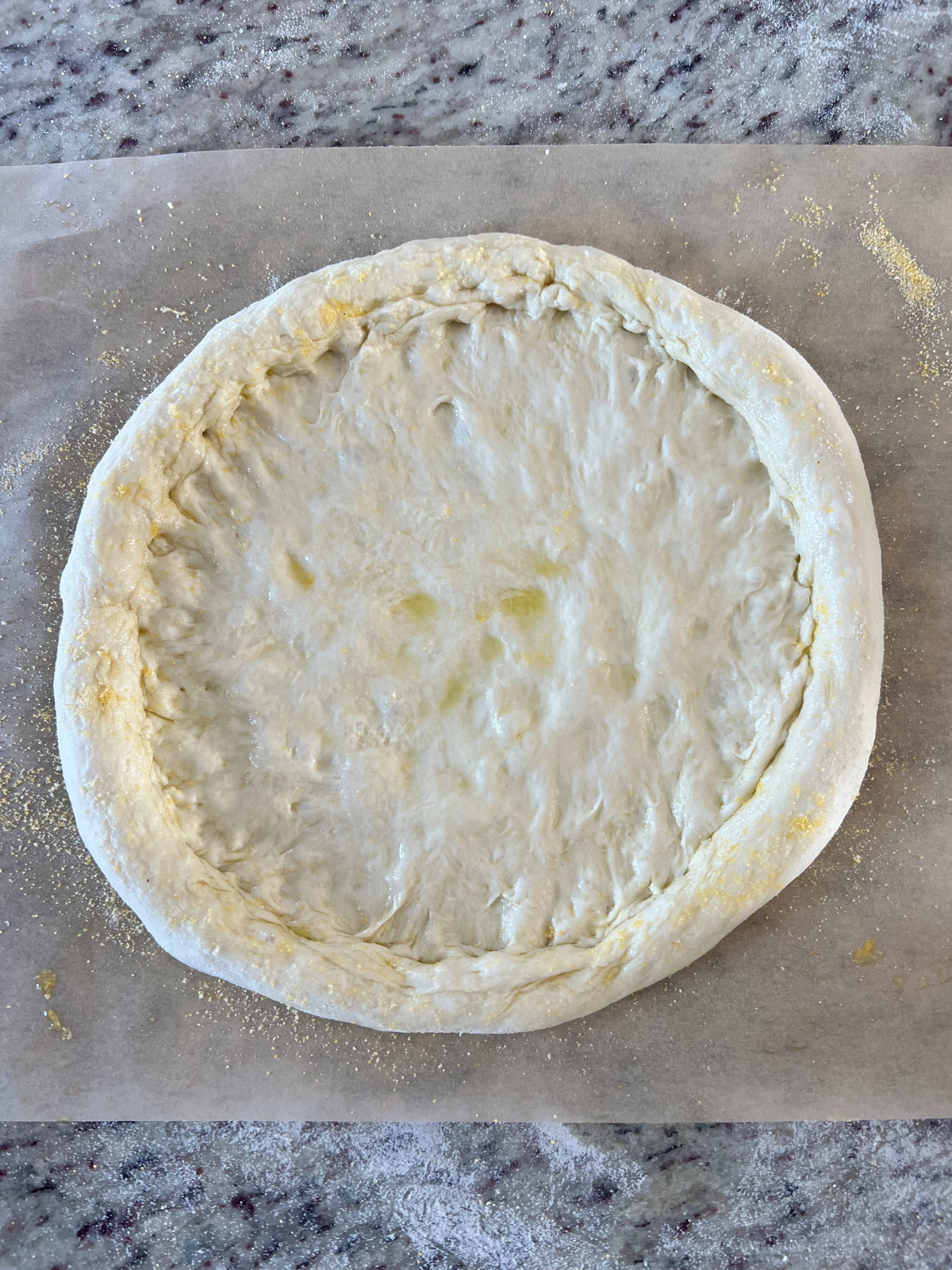 The sourdough pizza dough is shown shaped and sitting on parchment paper. 