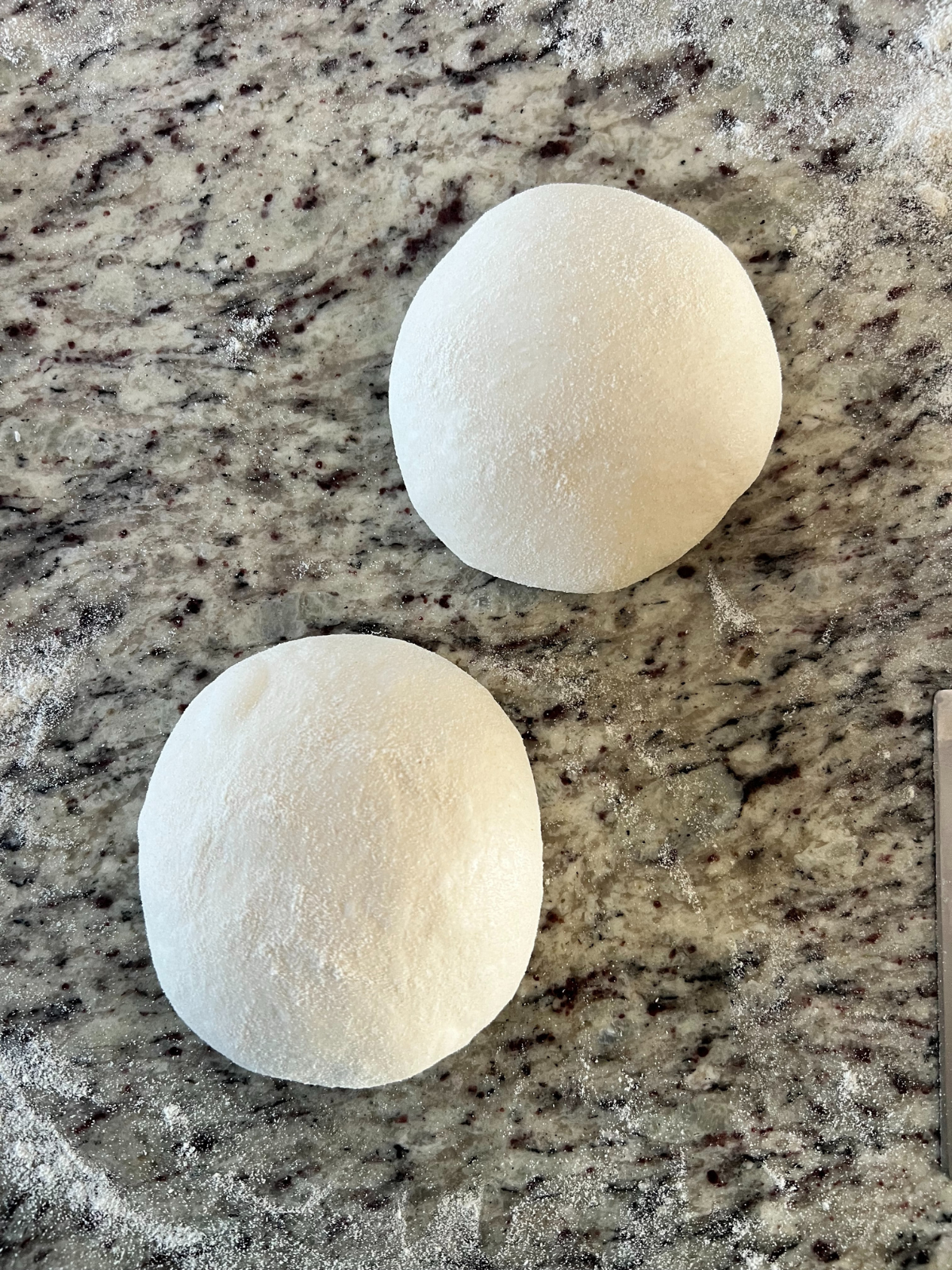 The sourdough pizza dough balls are divided into two dough balls and sitting on the counter. 