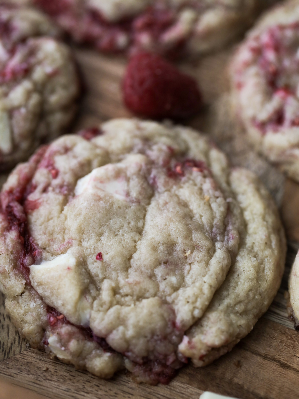 A closeup of one sourdough discard white chocolate raspberry cookie sits on a tray with several other cookies in the background.