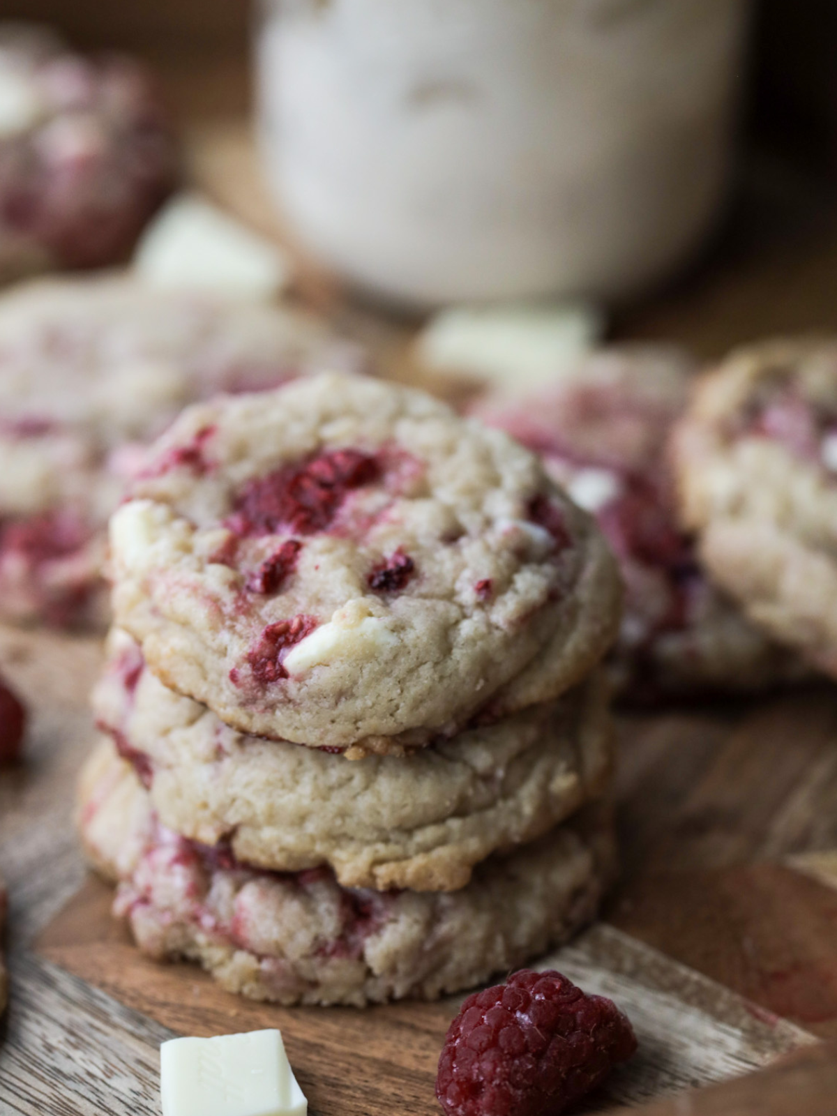 Three sourdough raspberry white chocolate cookies stacked on top of each other with several more cookies sitting in the background. 