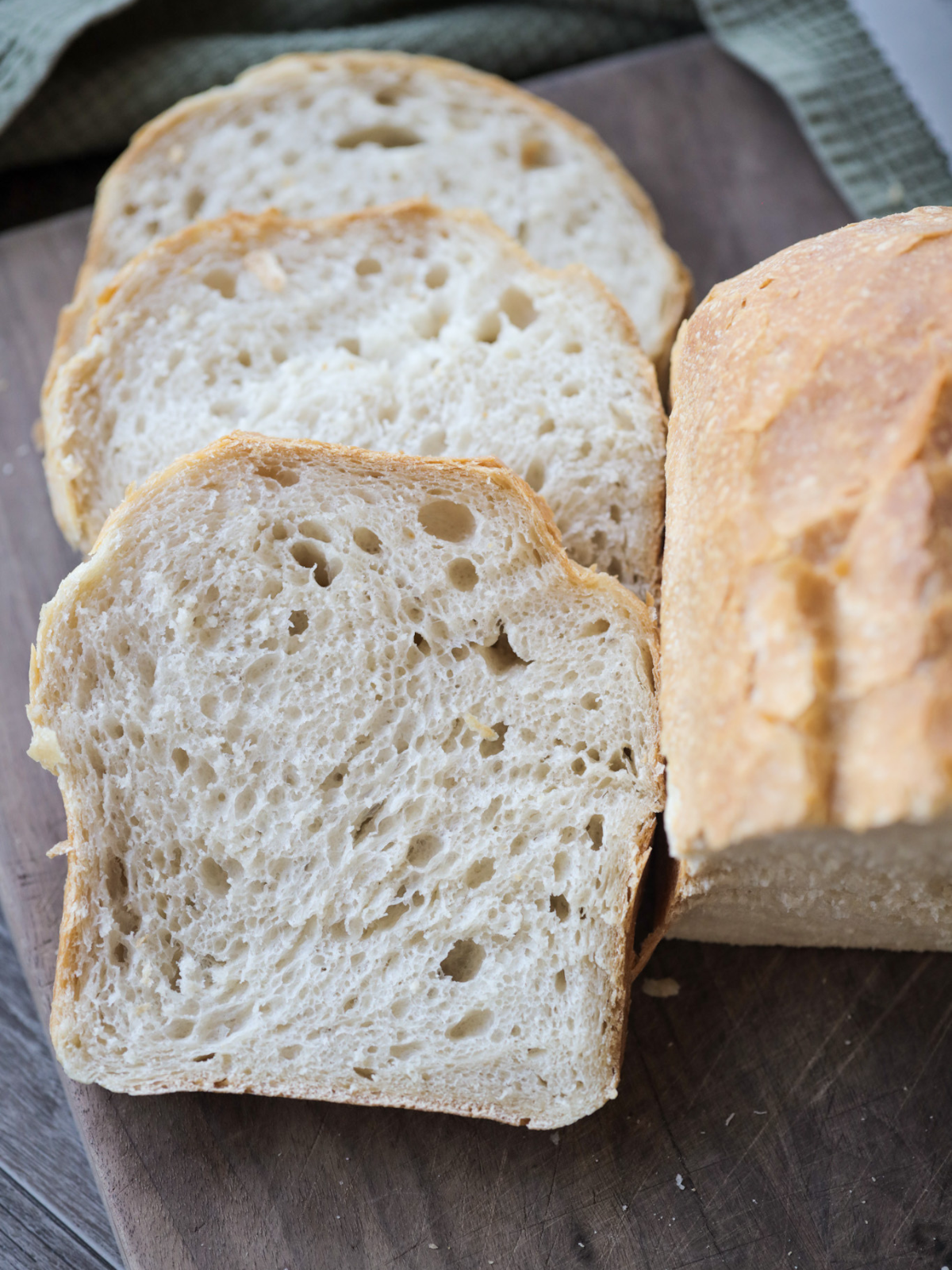 Three slices of sourdough sandwich bread sit on a wooden cutting board.