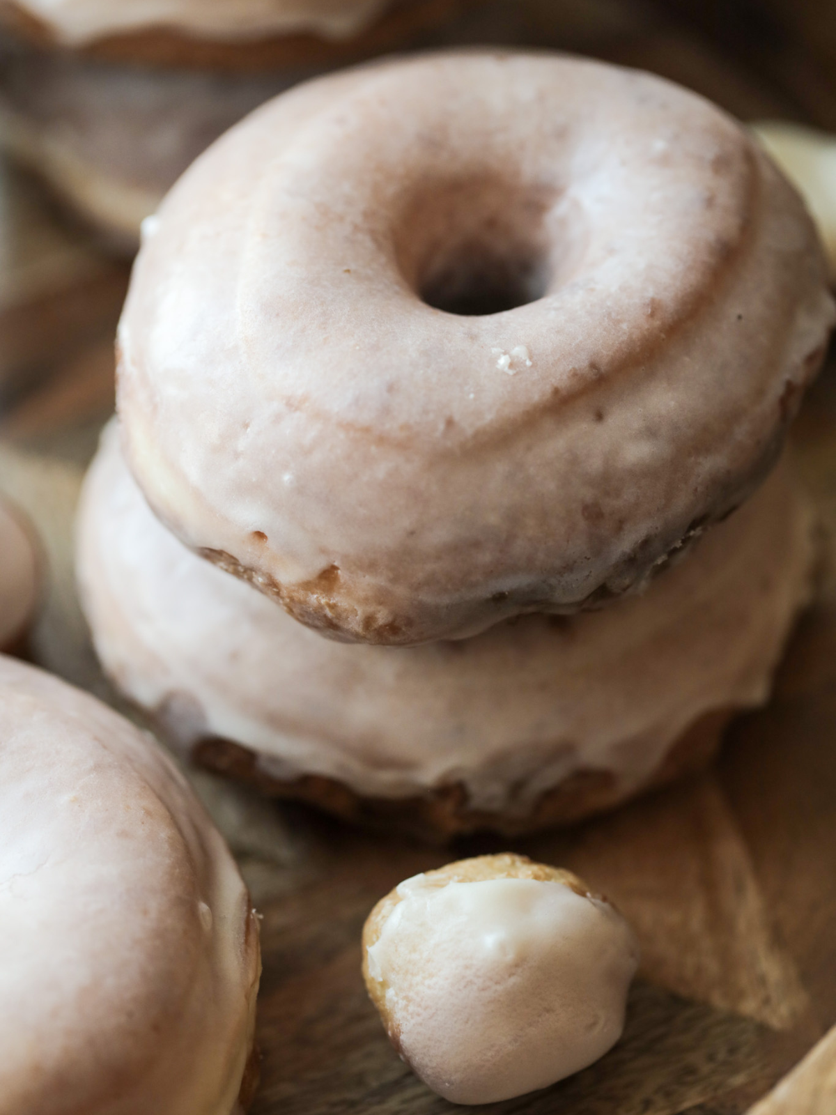 Two sourdough donuts lay on a wooden platter with several other sourdough donuts and donut holes in the background.