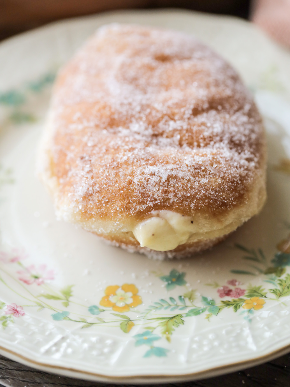 A vanilla bean custard filled sourdough donut sits on a vintage floral plate. 