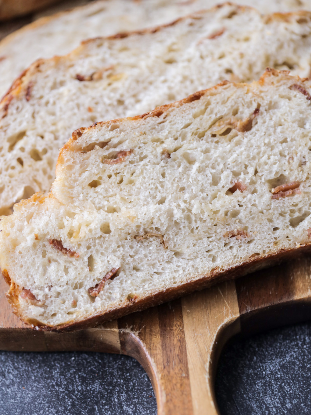 Three slices of sourdough bacon and gouda bread sit on a wooden cutting board.