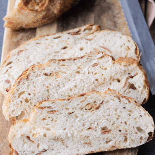 Three slices of sourdough smoked gouda and bacon bread on a wooden cutting board. The rest of the loaf sits in the background.