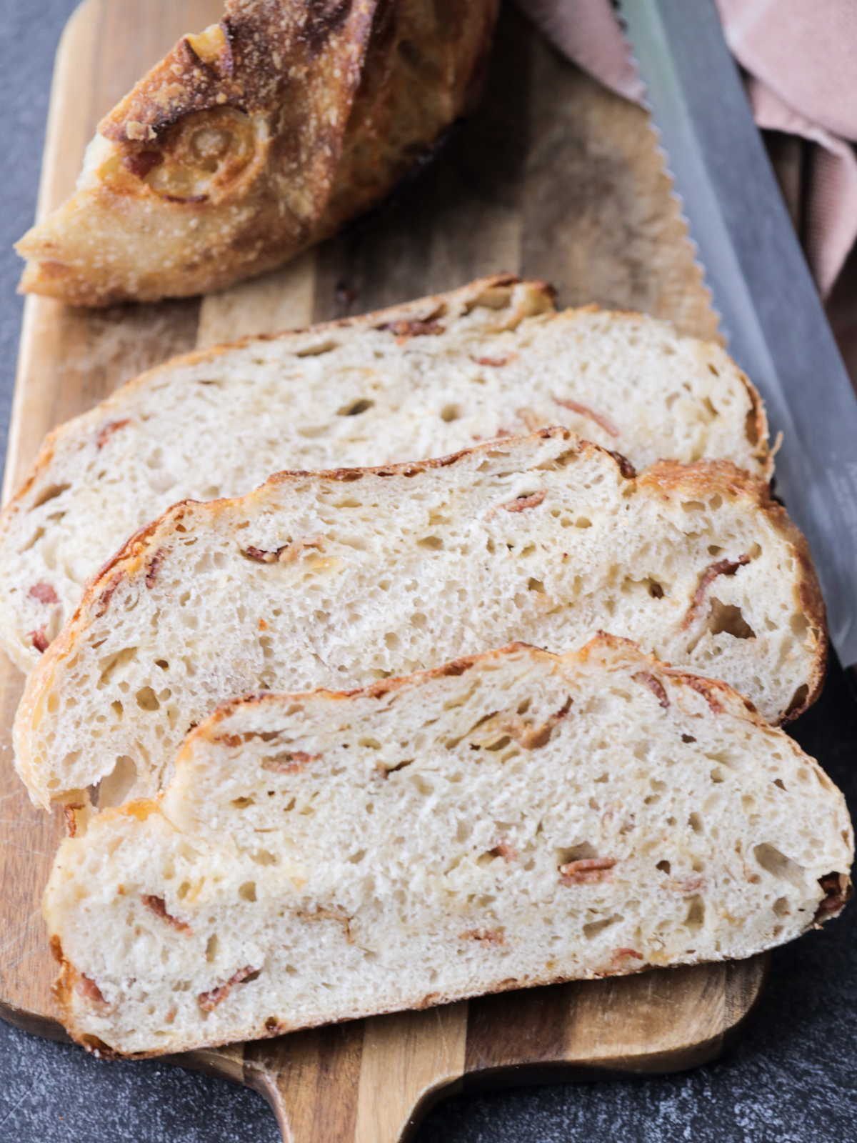 Three slices of sourdough smoked gouda and bacon bread on a wooden cutting board. The rest of the loaf sits in the background.