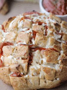 Cheesy pepperoni sourdough pull apart bread is shown sitting on a wooden cutting board with marinara sauce in the background.