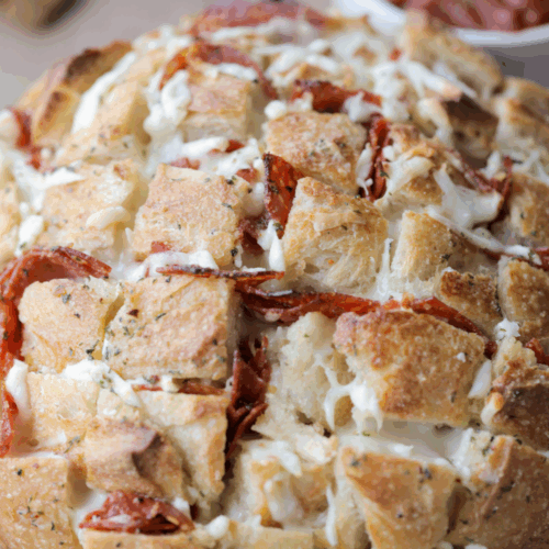 Cheesy pepperoni sourdough pull apart bread is shown sitting on a wooden cutting board with marinara sauce in the background.