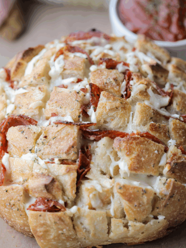 Cheesy pepperoni sourdough pull apart bread is shown sitting on a wooden cutting board with marinara sauce in the background.