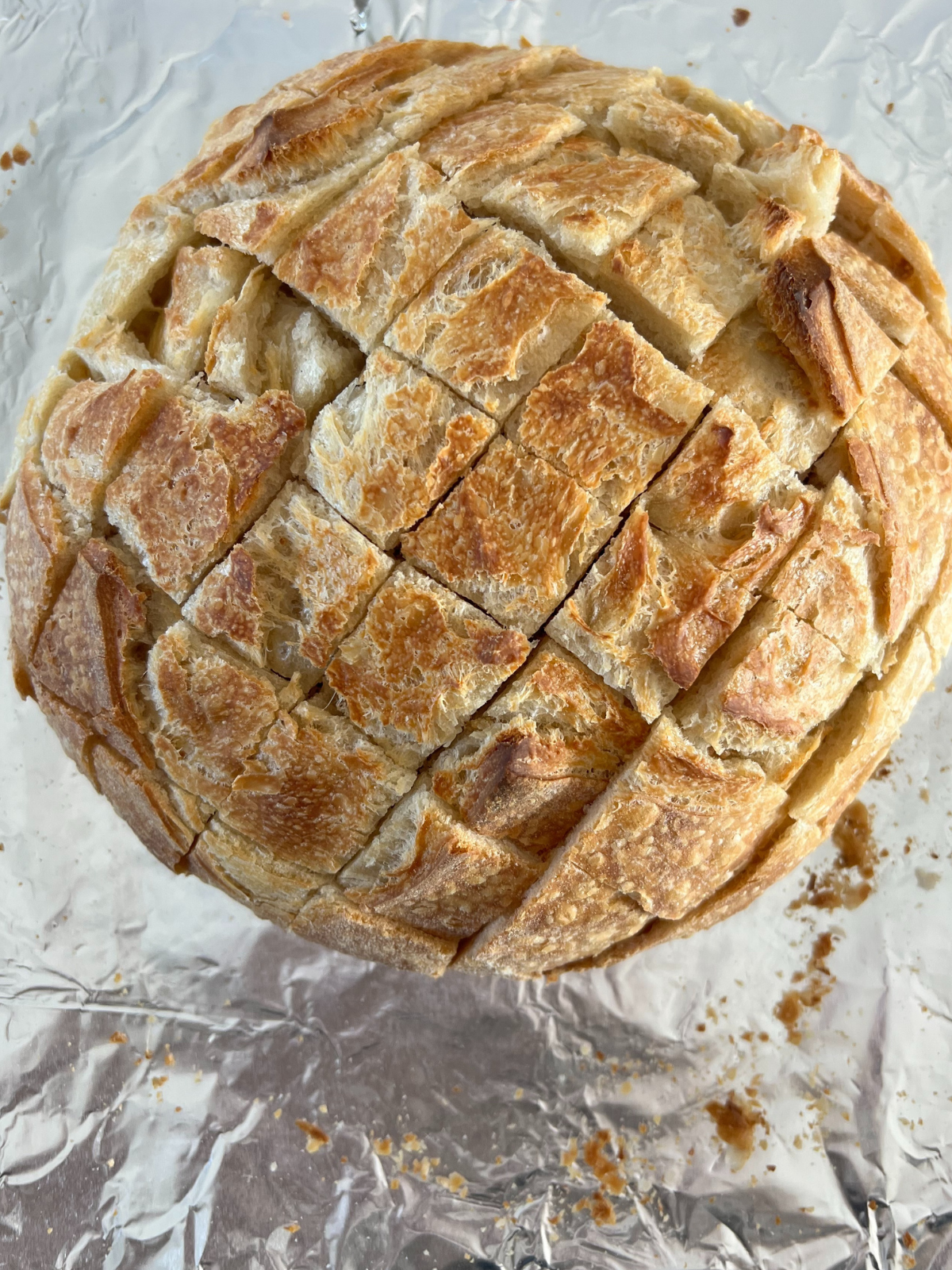 A loaf of sourdough bread sits on tinfoil with it cut into 1 inch pieces. 