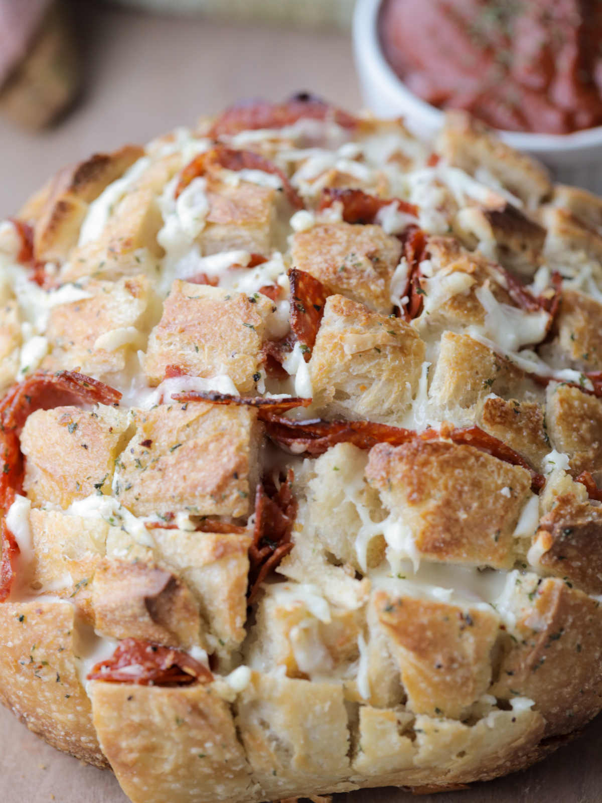 Cheesy pepperoni sourdough pull apart bread is shown sitting on a wooden cutting board with marinara sauce in the background.