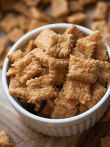 A bowl of sourdough homemade cheez-its sit on a platter with other cheez-its in the background.