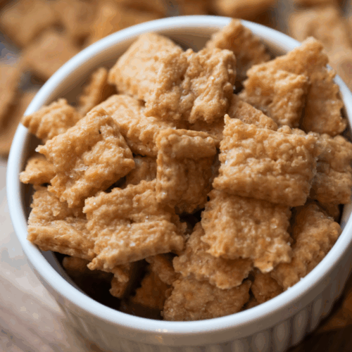 A bowl of sourdough homemade cheez-its sit on a platter with other cheez-its in the background.