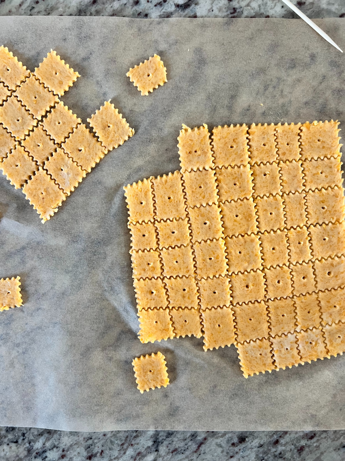 The unbaked sourdough cheez-its lay flat on parchment paper about to be baked.