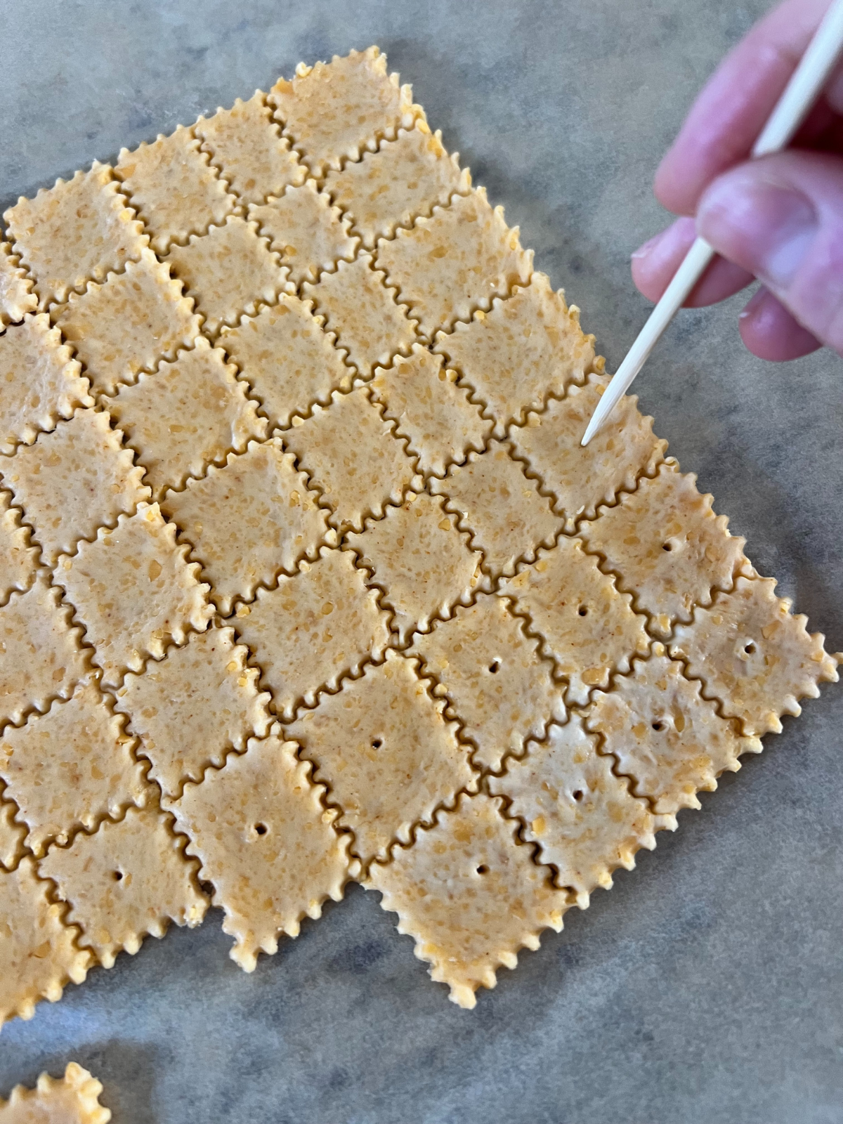 The rolled out sourdough cheez-it dough after being sliced into 1 inch squares. This picture shows me poking holes into the center of each cracker.