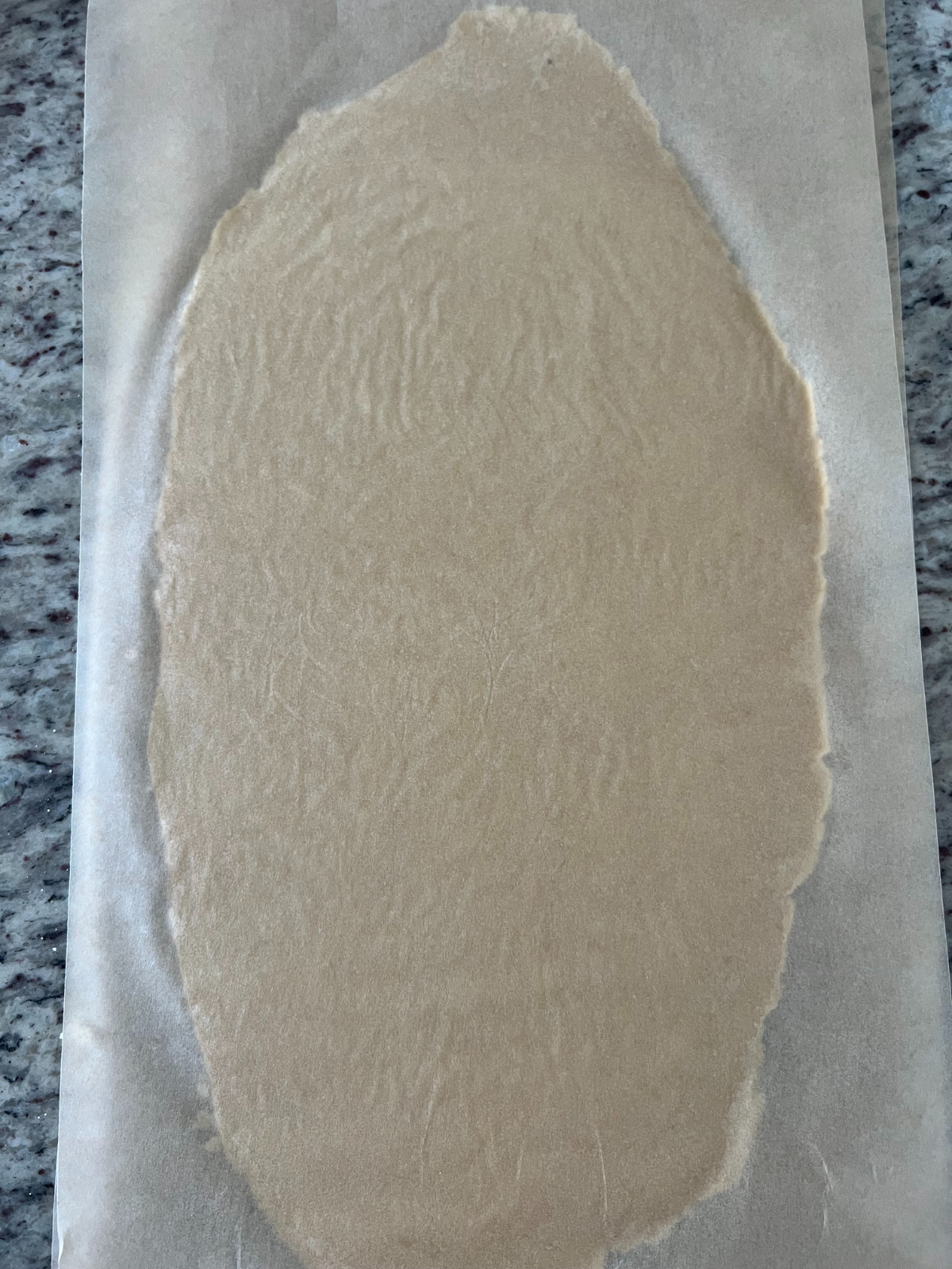 The sourdough discard sugar cookie dough has been rolled out between two sheets of parchment paper.