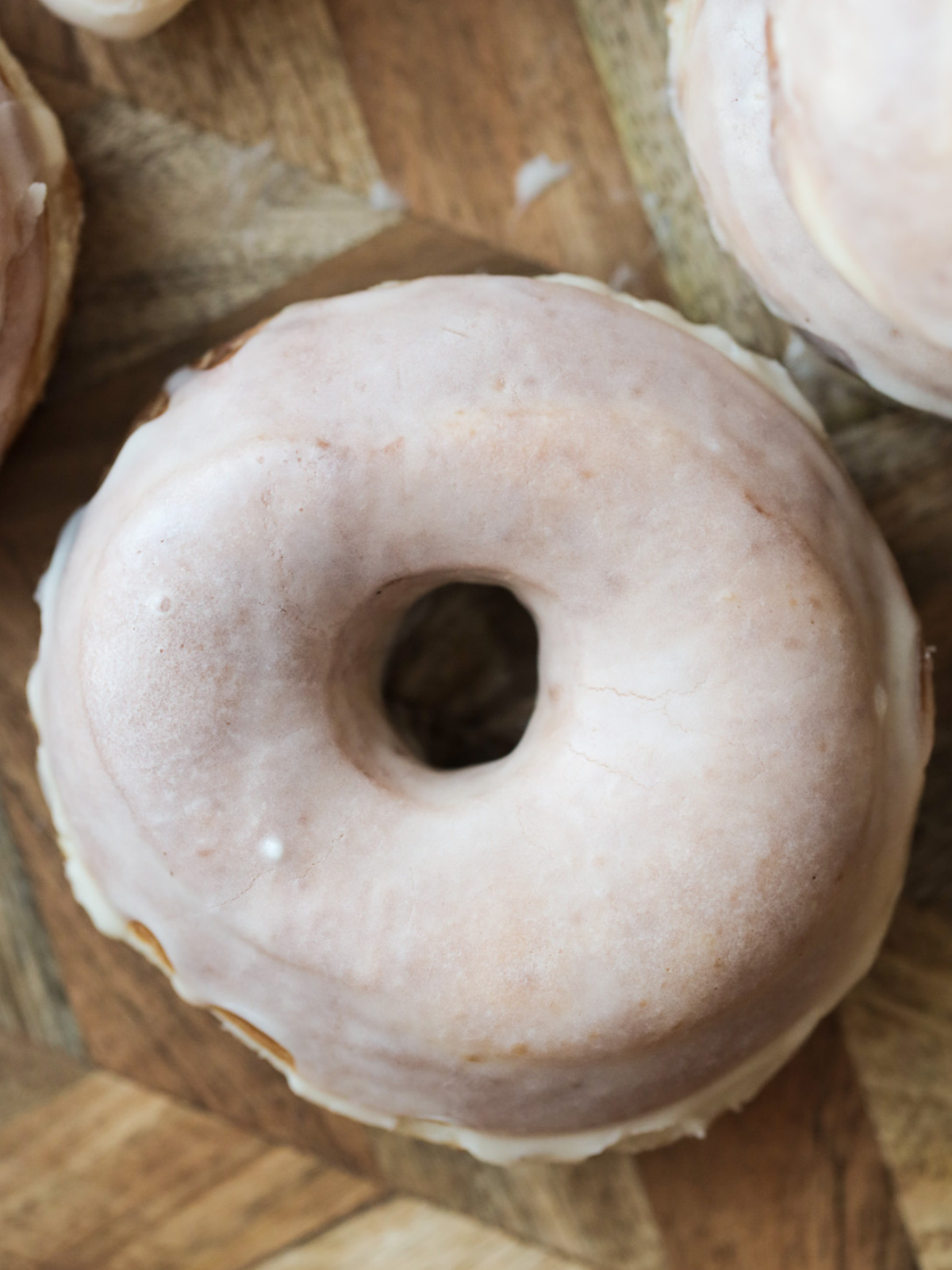 One closeup of a sourdough donut with glaze is shown surrounded by other donuts.